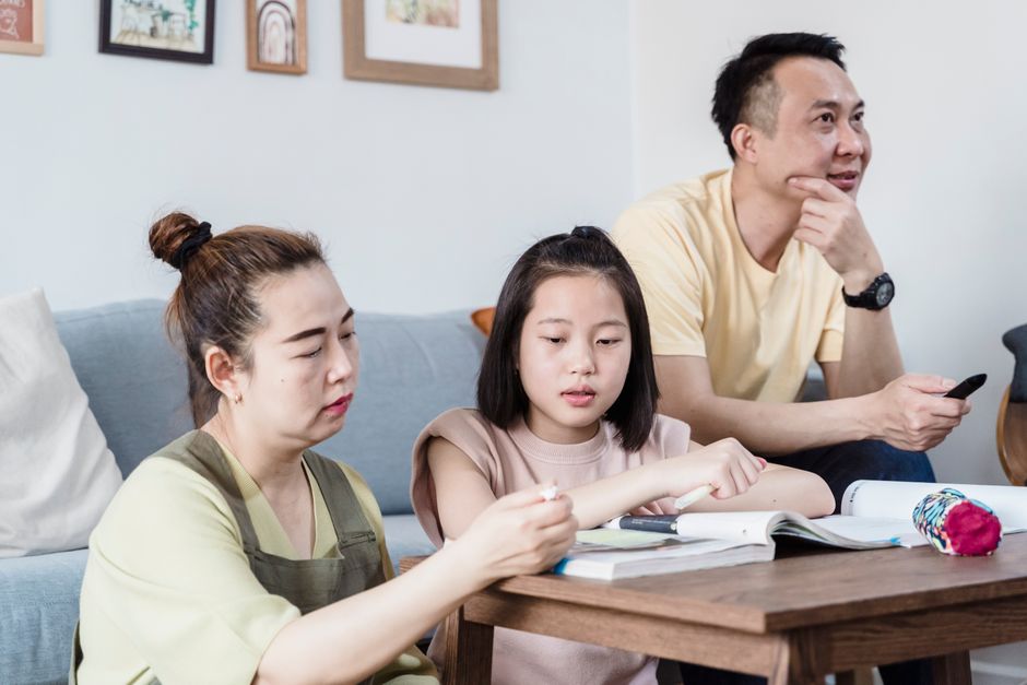 거실에서 가족이 딸의 숙제를 도와주며 함께하는 시간을 보내고 있습니다.