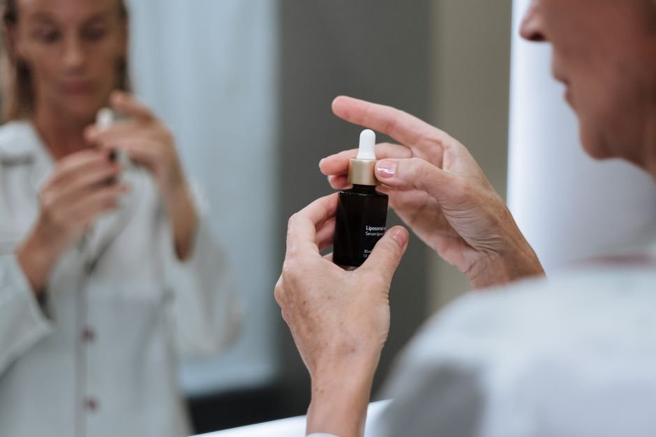 Senior woman applying skincare serum in front of mirror during morning routine.