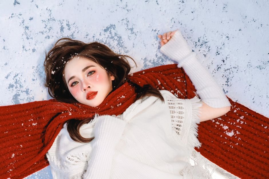 빨간 스카프를 두른 채 눈 위에 누워 있는 여성의 아름다운 겨울 초상화입니다.